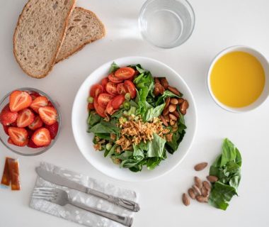 Top view of a healthy salad and fresh ingredients with bread and juice on a white surface.